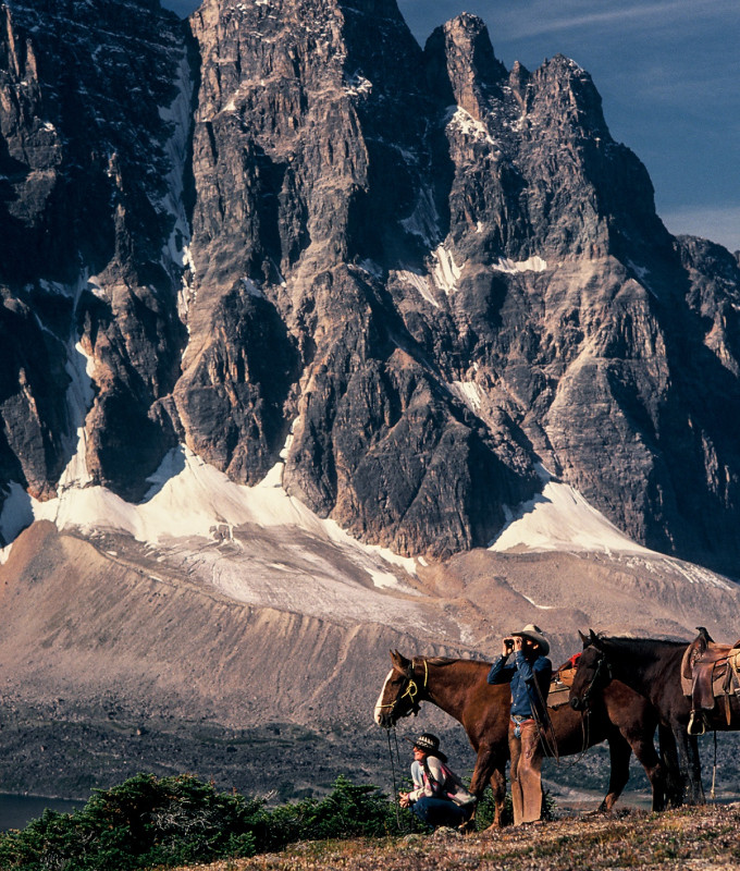 Cowboy looking through binoculars with horses and mountains